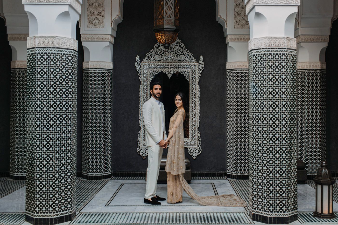 Couple standing between ornate Moroccan-style pillars with geometric patterns.