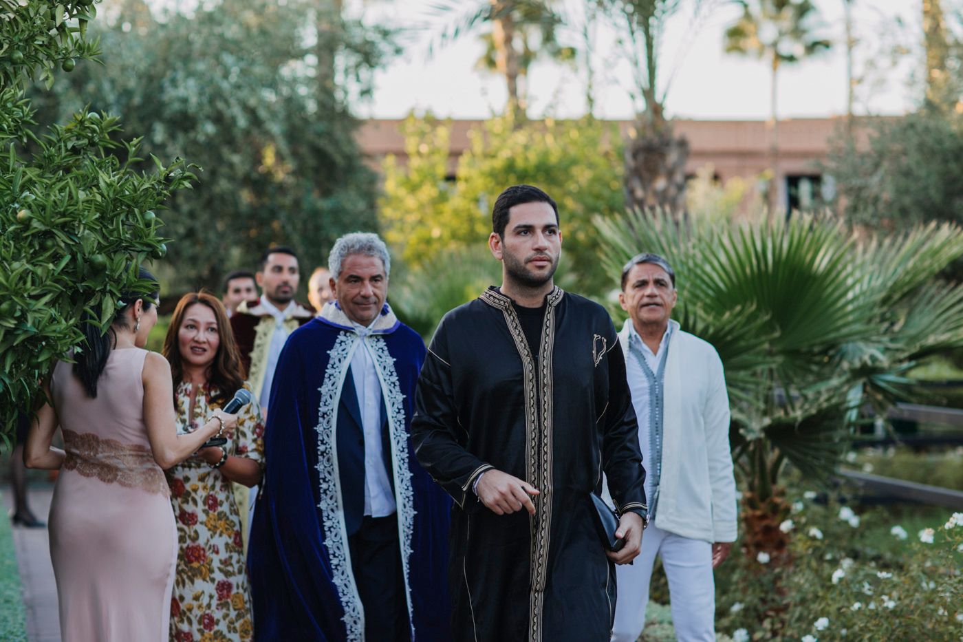 Wedding guests gathered in lush garden setting with palm trees and formal attire.