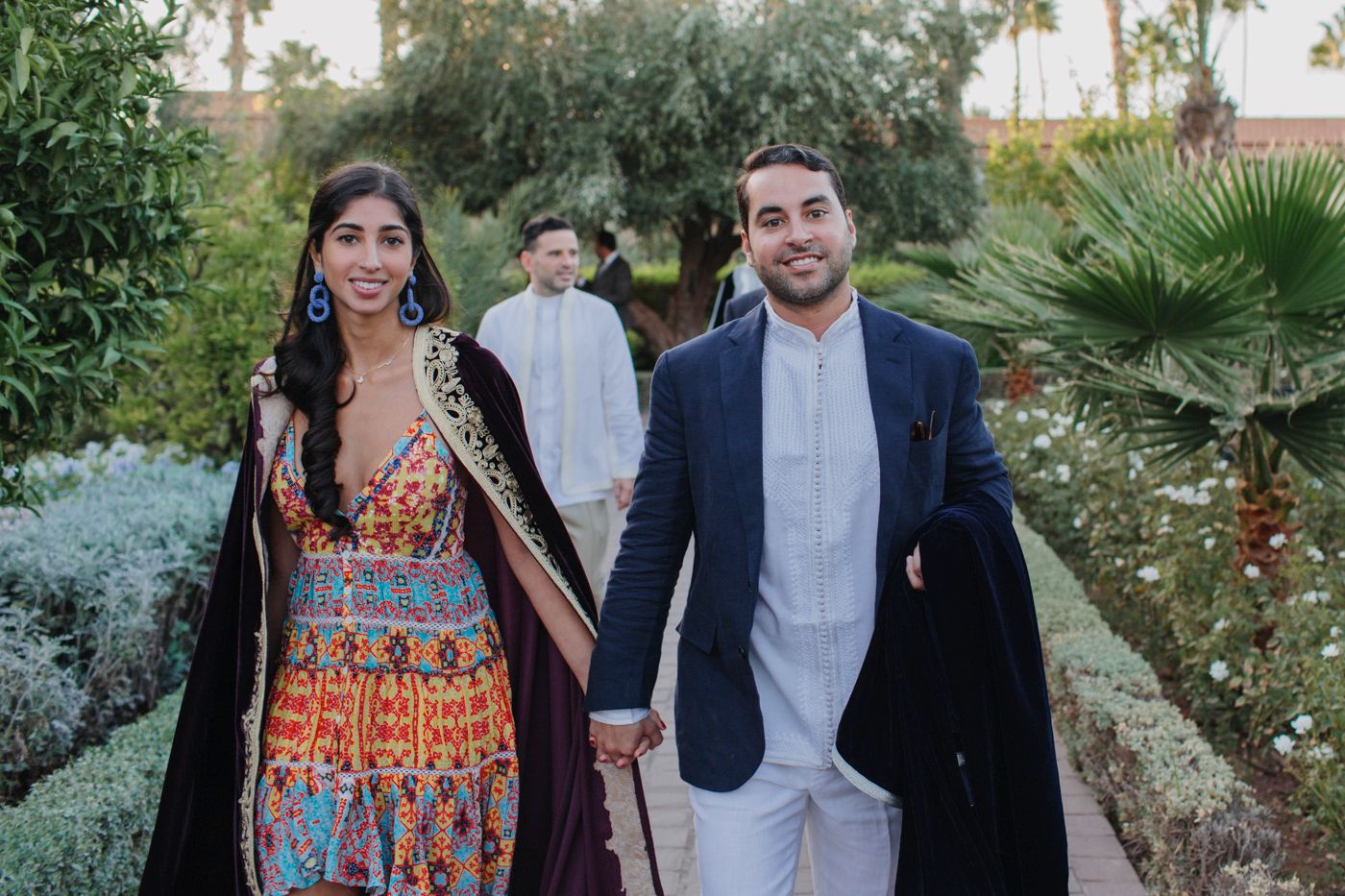 Couple walking hand in hand through tropical garden setting in formal attire.