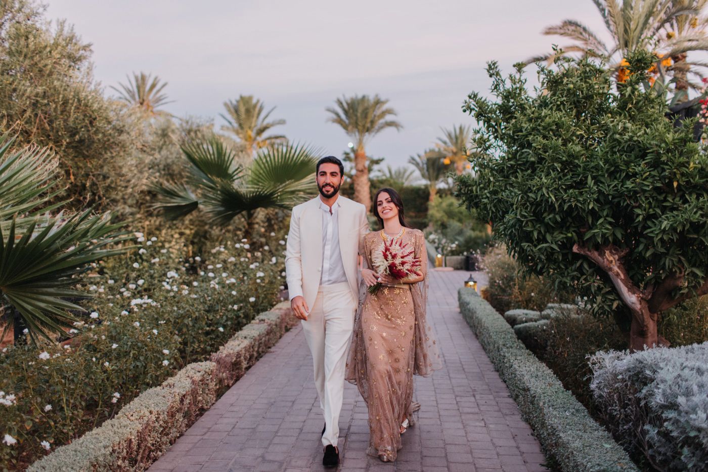 Couple walking along garden path surrounded by palm trees and tropical landscaping.