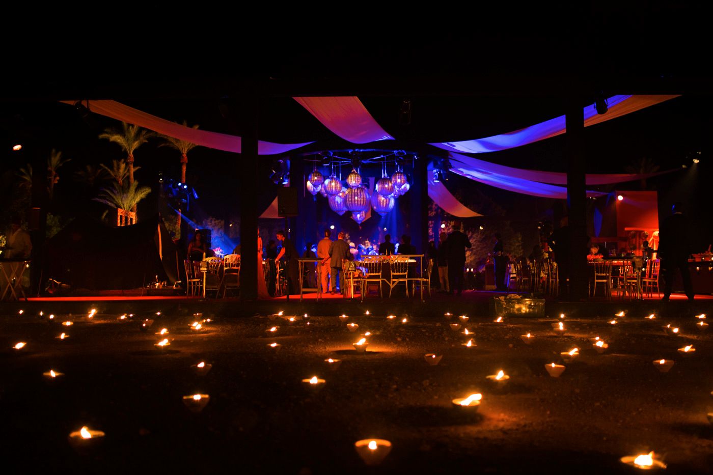 Outdoor venue decorated with candlelight and colorful stage lighting creating a magical nighttime atmosphere.