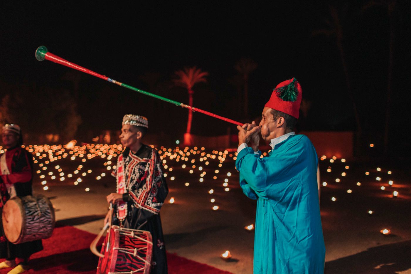 Musicians in traditional dress perform with colorful instruments during an evening celebration.