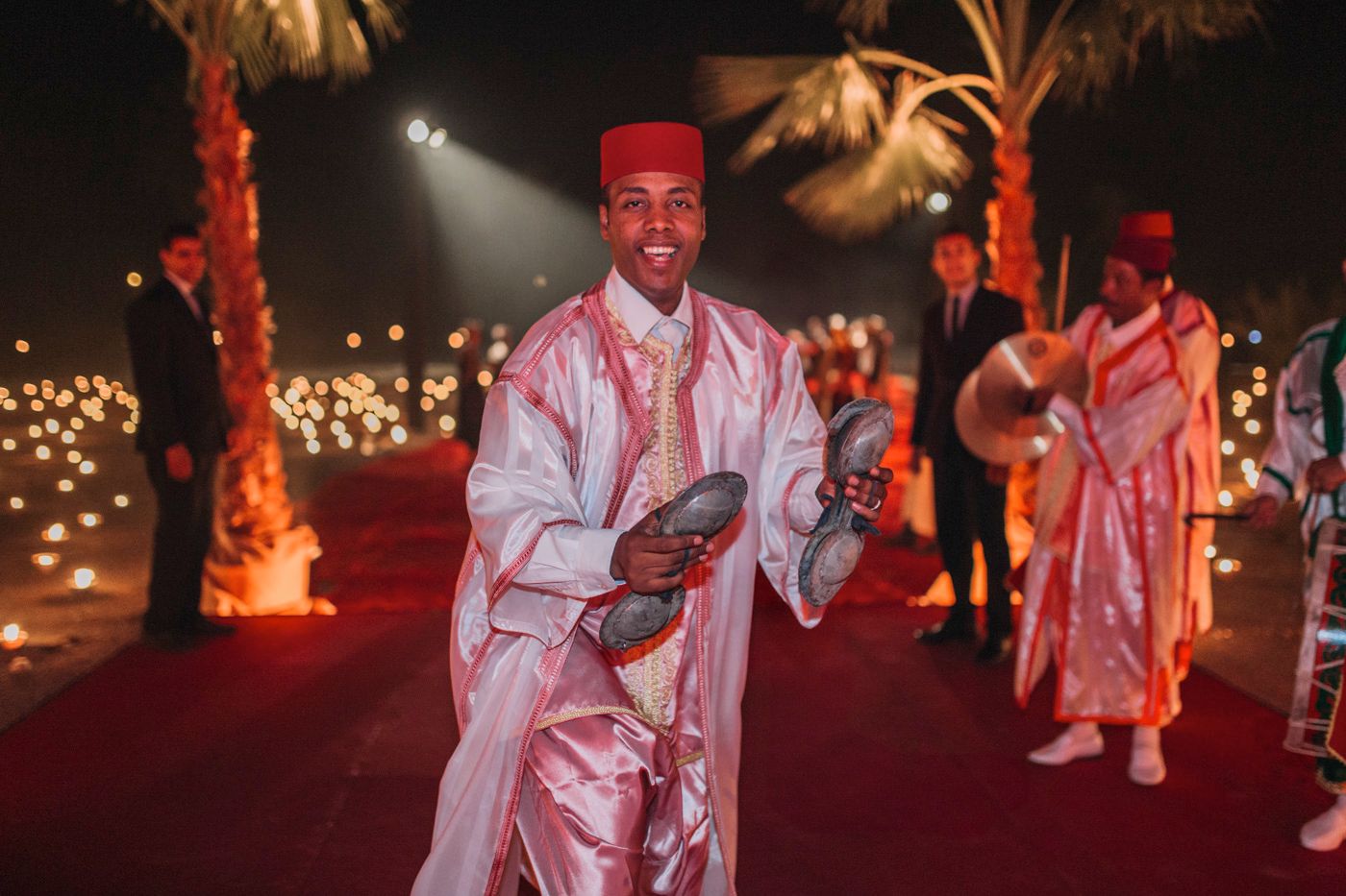 Performer in traditional white Moroccan attire plays music during nighttime celebration.