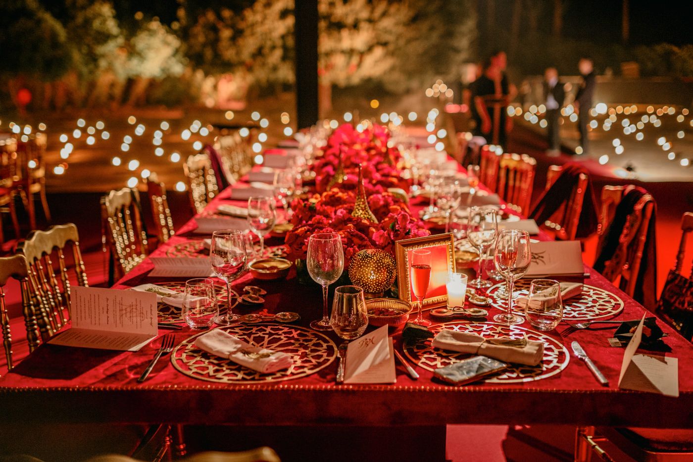 Long banquet table decorated with red floral arrangements and candlelight for evening reception.