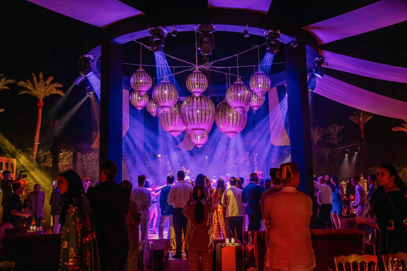 Purple-lit event space with hanging lanterns and palm trees creating a magical atmosphere.
