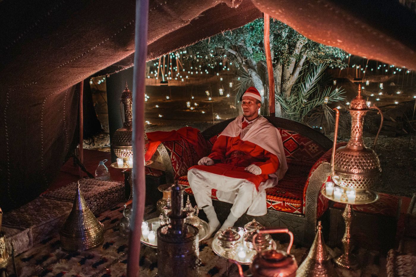Person dressed as Santa Claus sits in a decorated lounge area with lanterns and holiday decor.