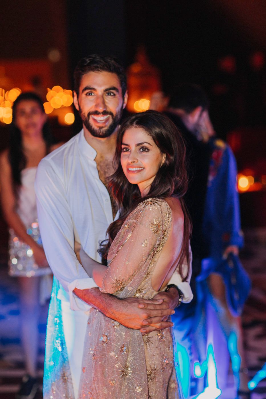 A couple embraces on the dance floor at a party with warm lighting and festive atmosphere.
