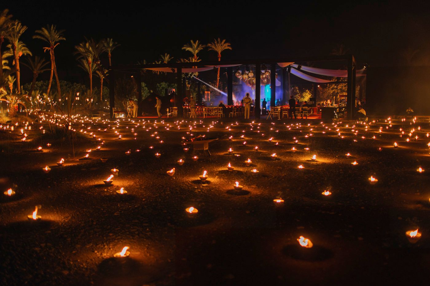 Outdoor event space decorated with hundreds of glowing candles and palm trees under the night sky.