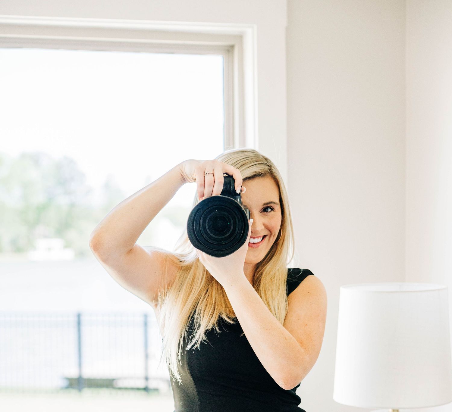 Preslee McGough - Professional photographer holding digital camera in bright indoor studio setting.