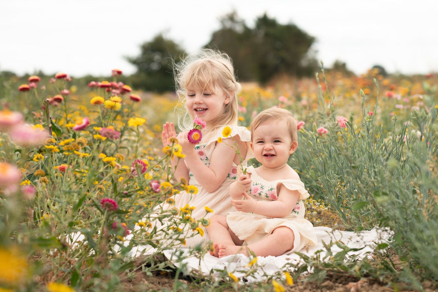 Two sisters sat together in a flower field smiling