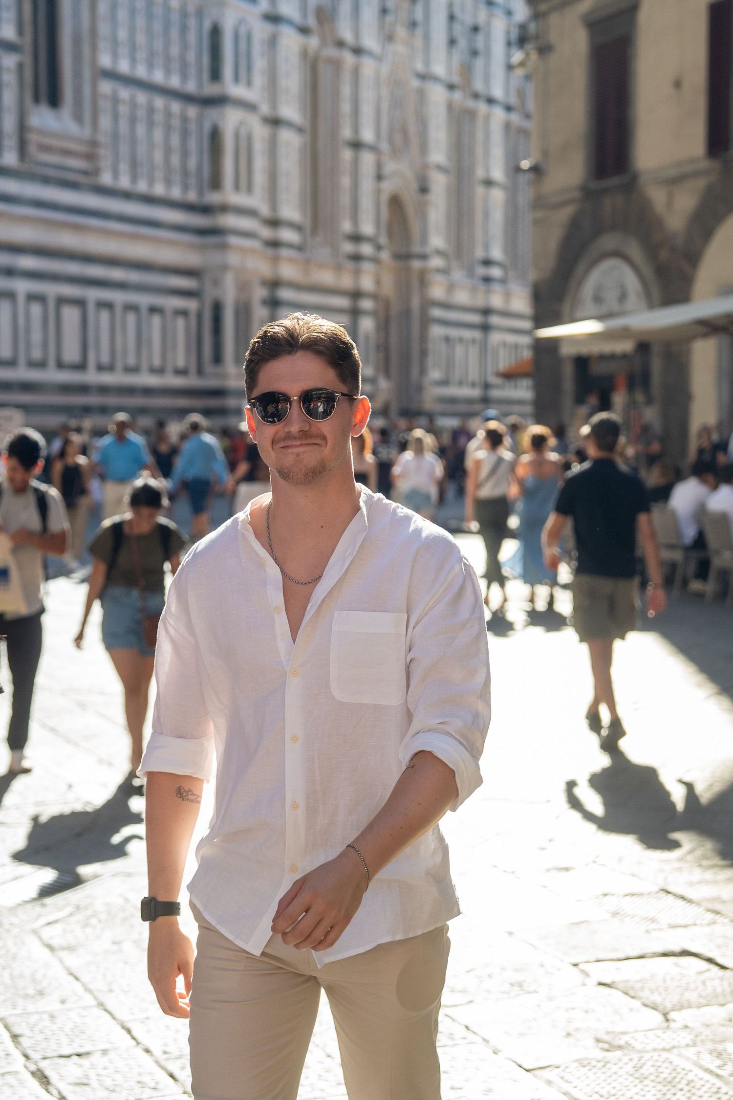 A young man walking towards the camera whilst backlit from the sun in a crowed Italian city