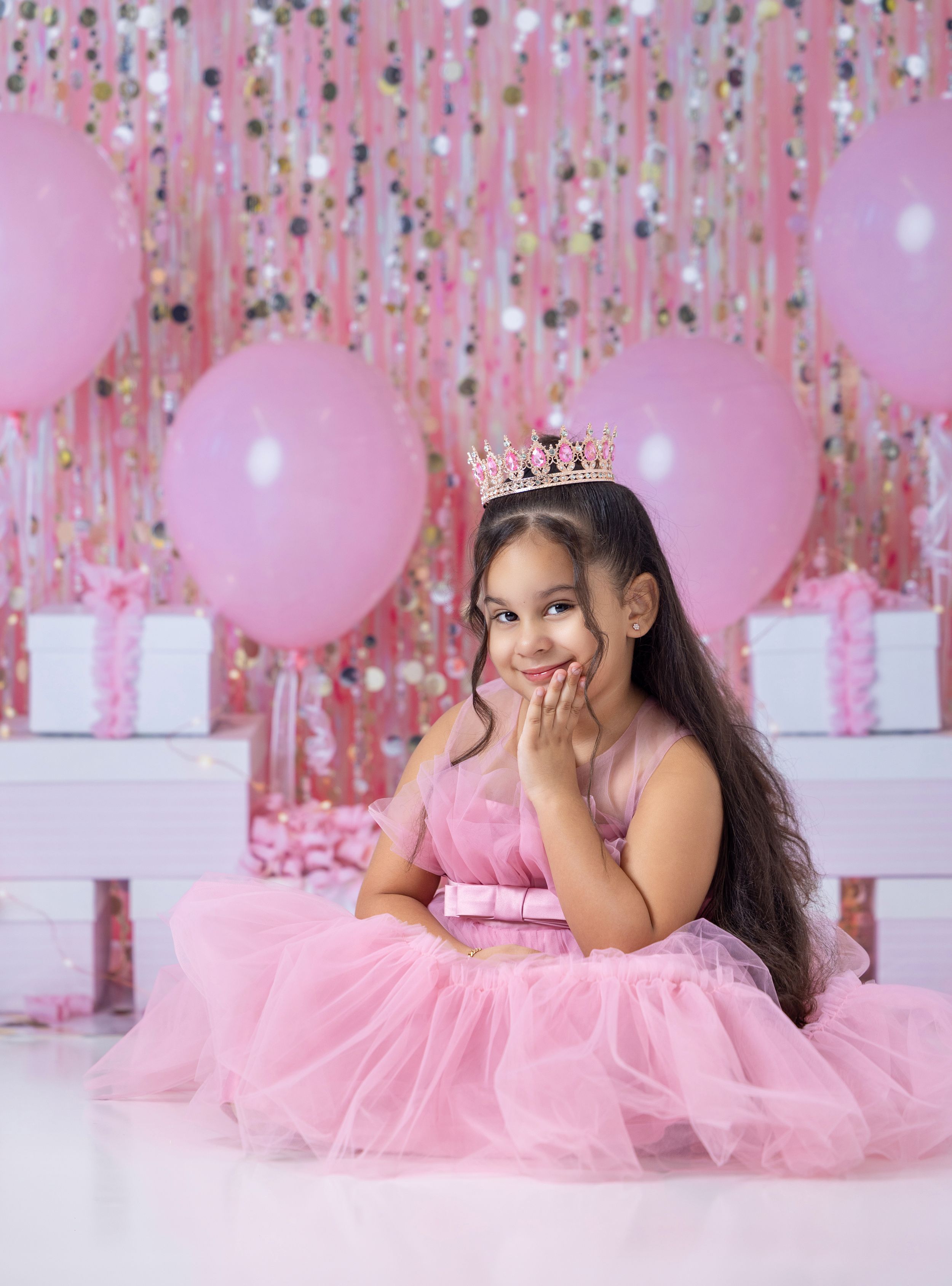 Young girl in pink tutu dress and crown poses with gifts and balloons in a pink birthday photo shoot.