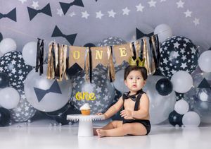 Baby's first birthday cake smash with black and white star balloons, ONE banner, and gold crown decorations.