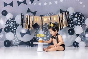 Baby's first birthday cake smash with ONE banner, star balloons, and gold crown on white backdrop.