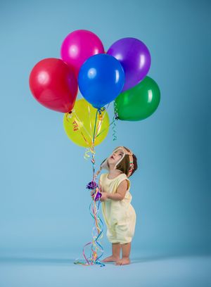 Young girl in yellow dress holding colorful balloons on blue background.