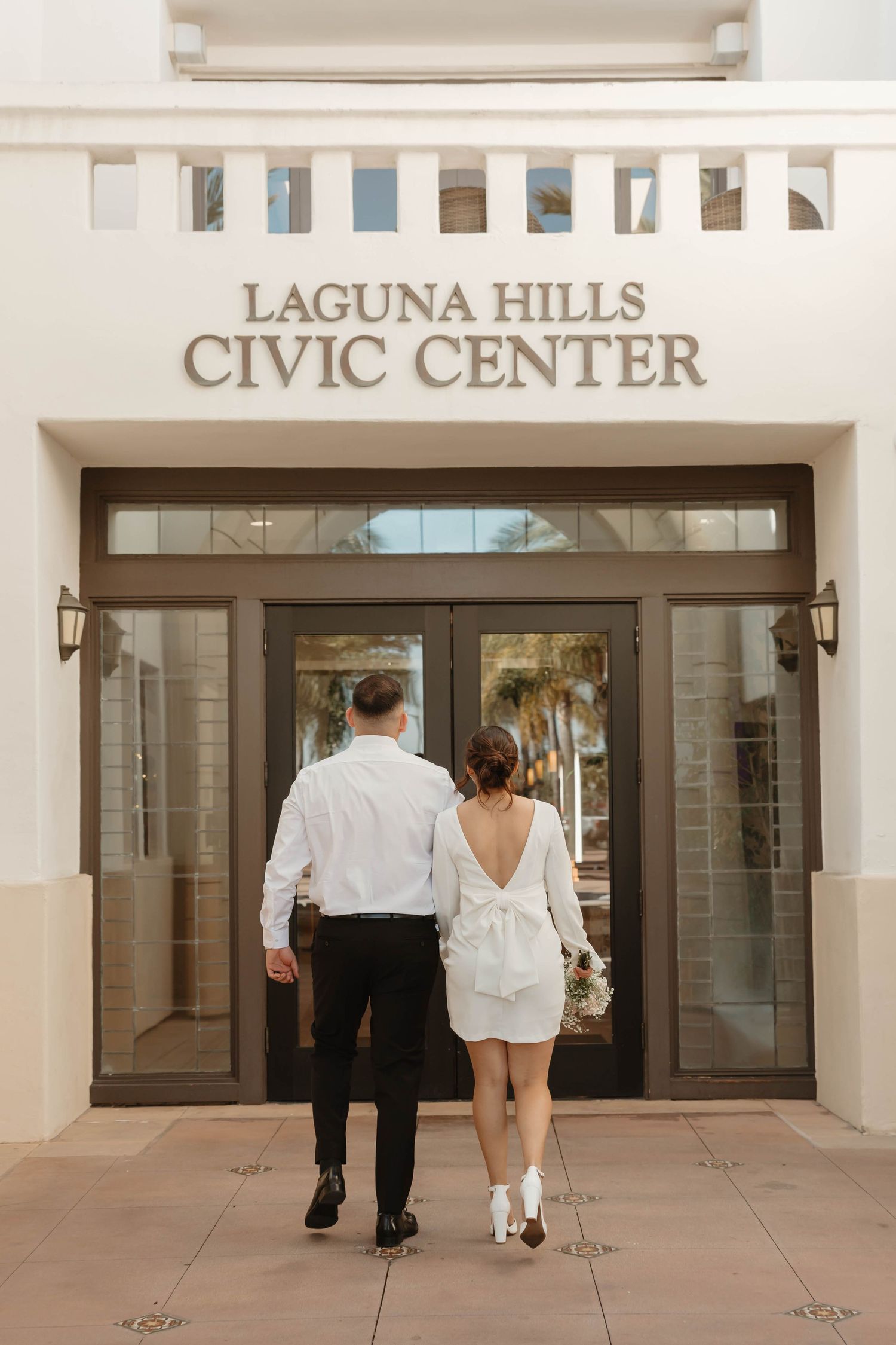 A couple walks away from the camera towards the entrance of the Laguna Hills Civic Center building.