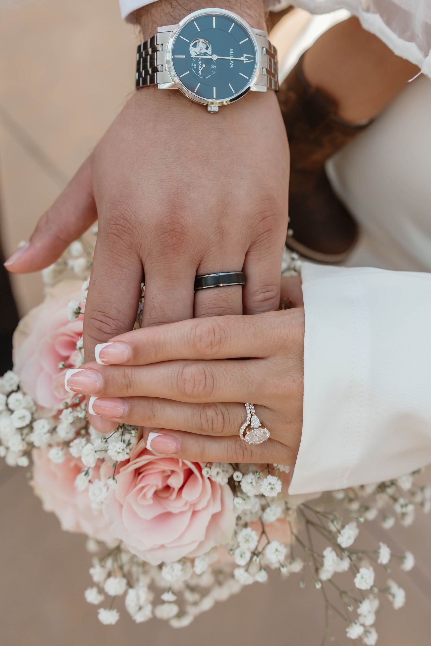 Close-up of hands with engagement ring and watch against pink roses and baby's breath flowers.