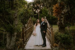 Bride and groom posing on a rustic wooden bridge surrounded by lush tropical greenery on their wedding day.