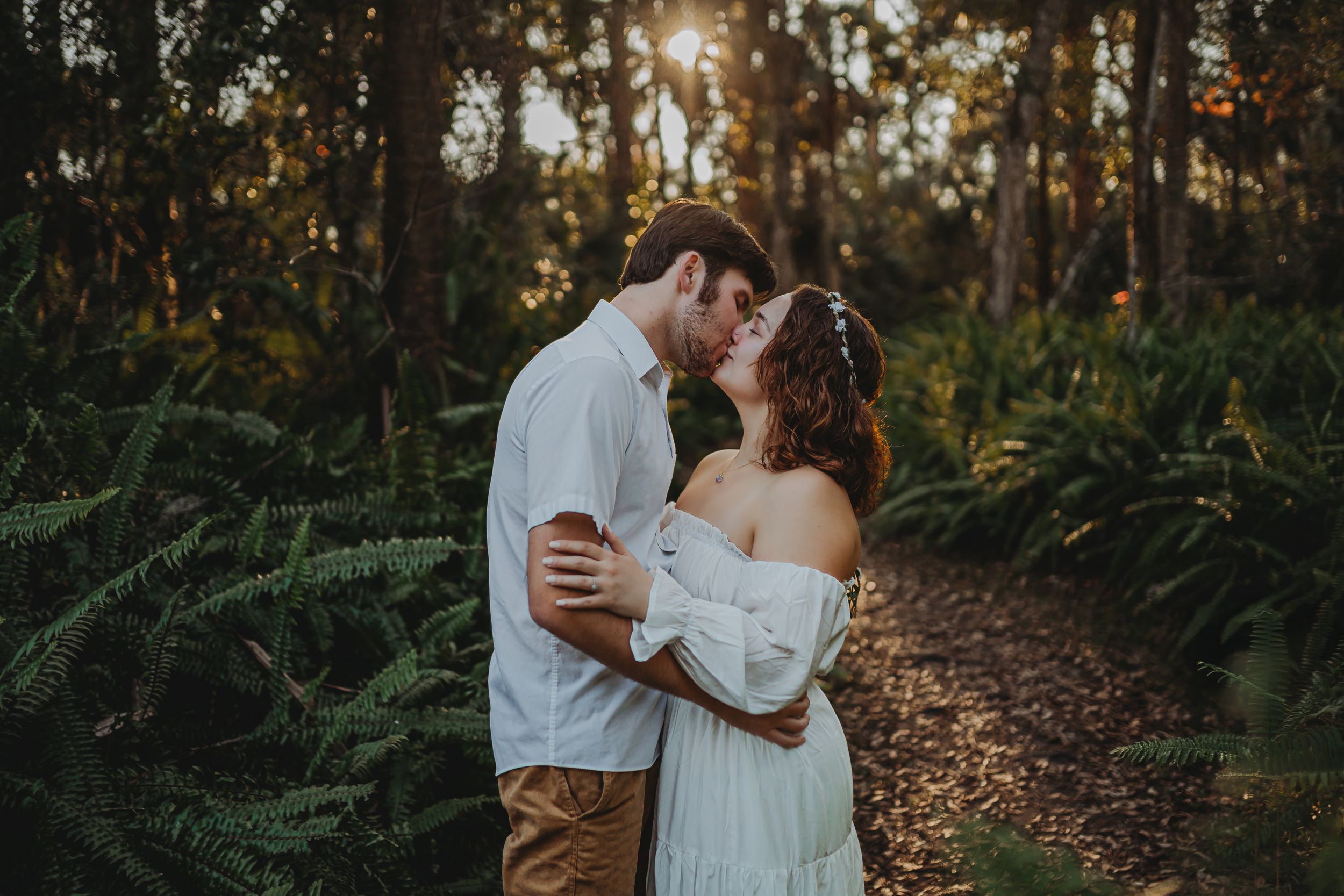A romantic couple embraces in a sunlit forest path surrounded by lush ferns during golden hour. Cape Coral Florida, SWFL photographer,