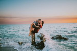 A romantic couple embraces in ocean waves during a vibrant sunset with orange and blue sky. Venice Beach Florida, Swfl