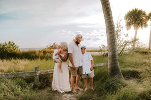 Family of four enjoying a golden sunset beach moment near palm trees and coastal grasses on a sandy path.