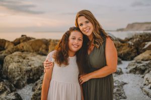 Two people pose together on coastal rocks during sunset with cliffs in background.