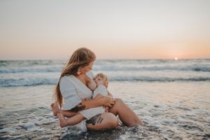 A tender moment between parent and child sitting together on beach at sunset.