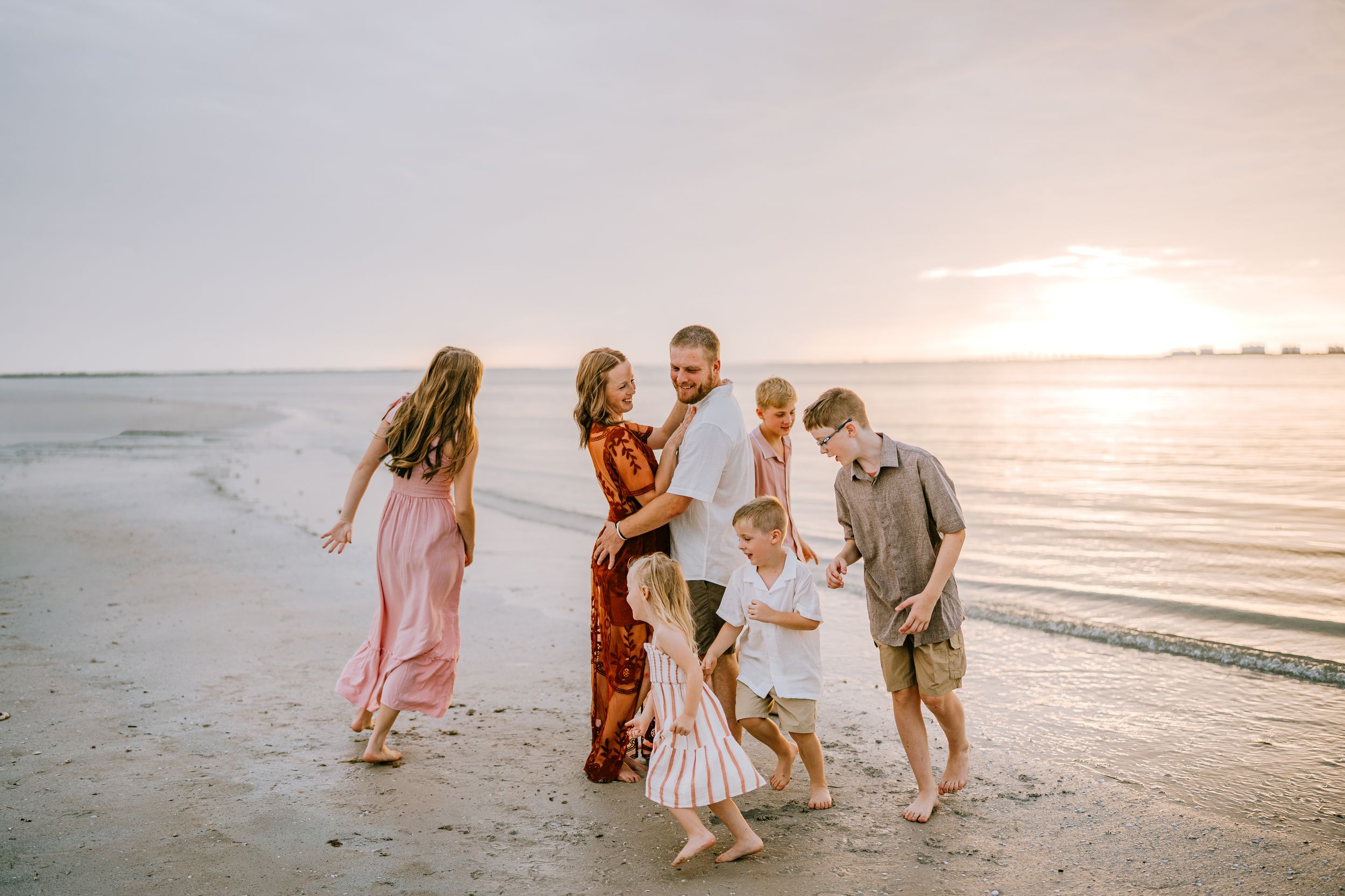 Family of six enjoying a sunset beach walk together, with waves and golden sky in the background.