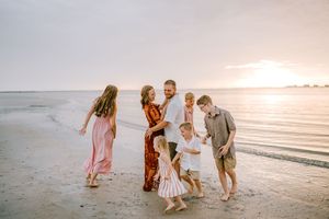 Family of six enjoying a sunset beach walk together, with waves and golden sky in the background.