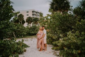 Couple embracing on a sandy beach path surrounded by lush greenery during a maternity photoshoot in Florida.