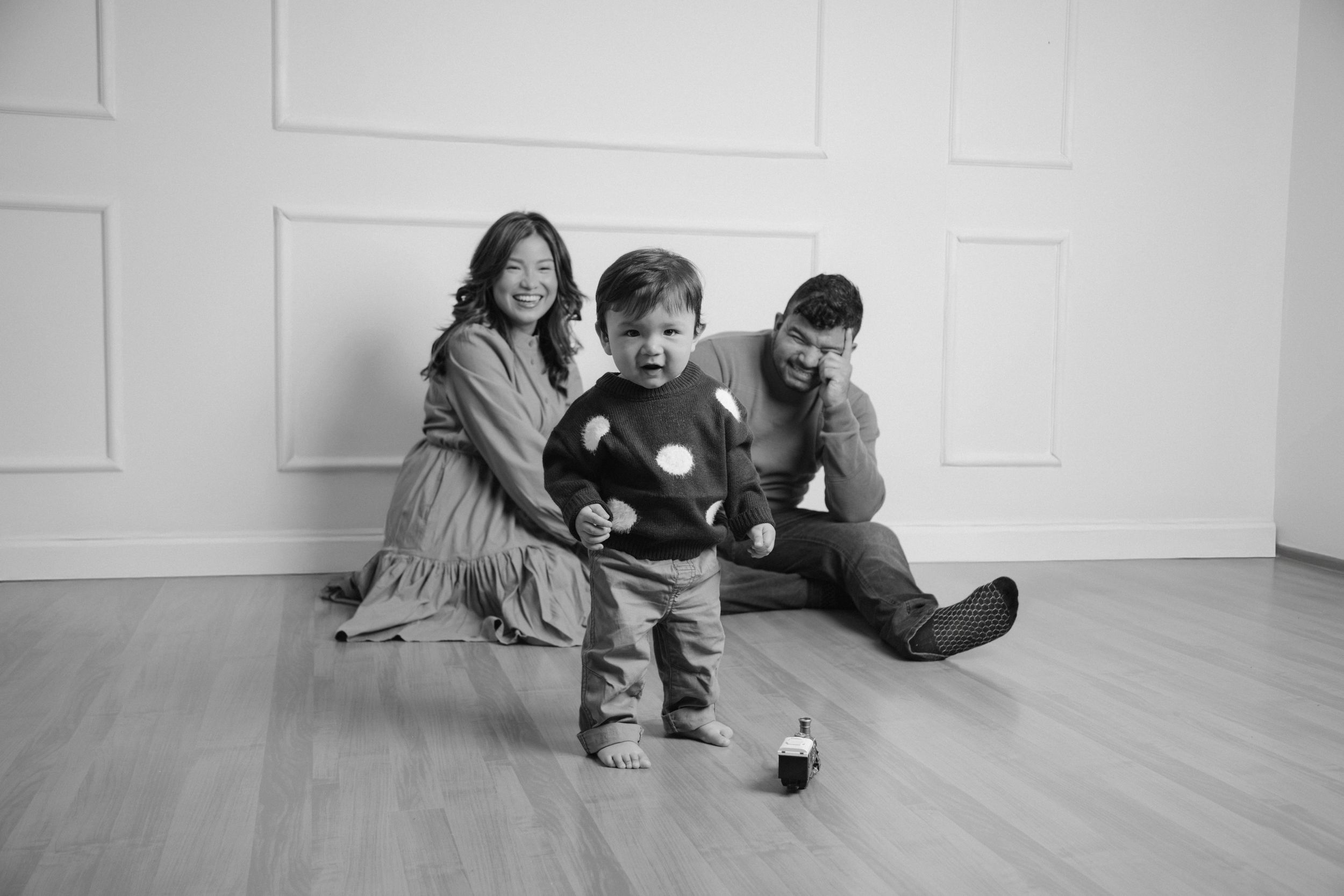 Family plays together on hardwood floor in bright white room during lifestyle session.