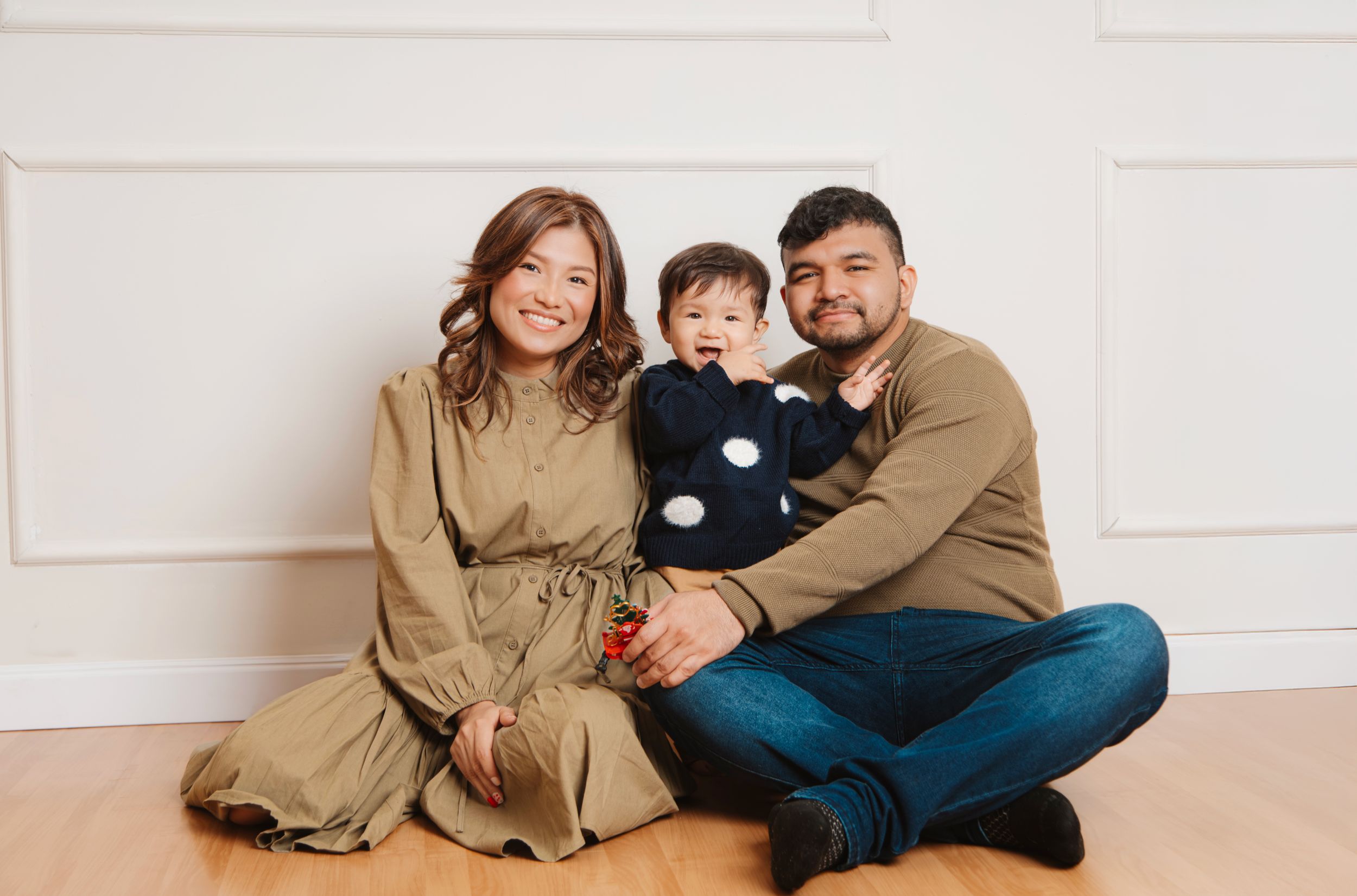 Family in coordinating neutral outfits sitting together on wooden floor for portrait session.