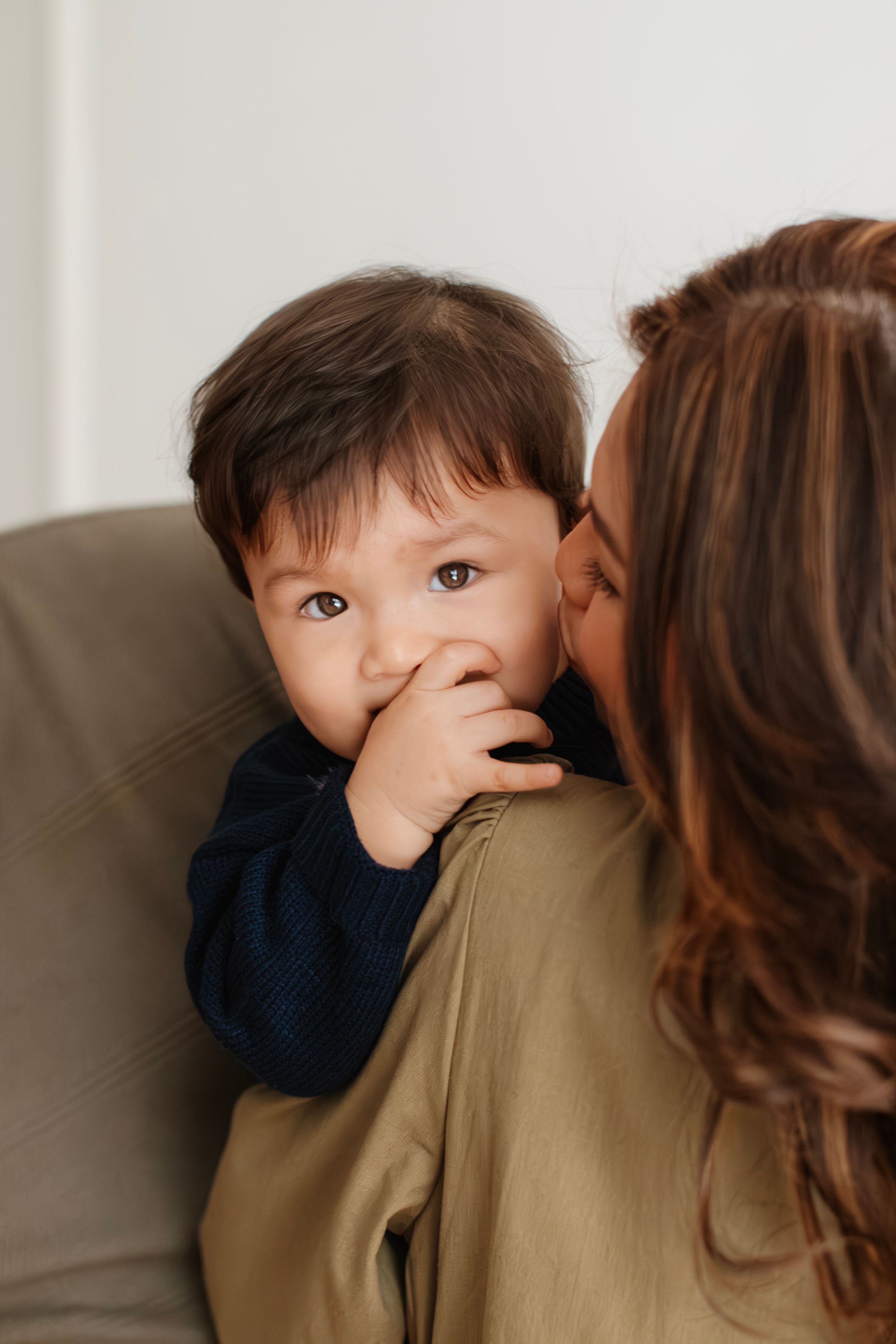 Candid emotional moment between a young child and adult being affectionate on a grey couch.