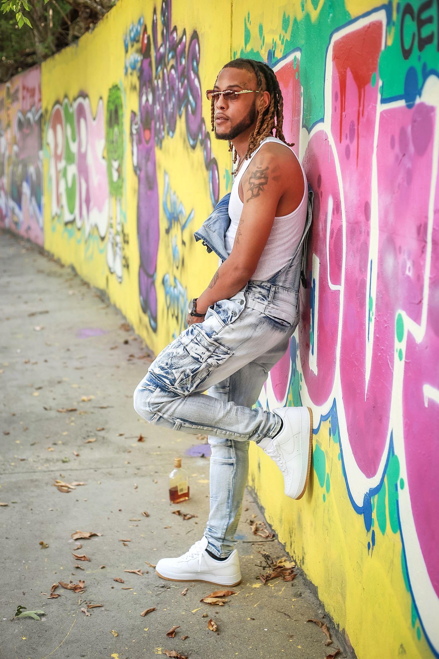 Urban fashion portrait against colorful graffiti wall with white tank top, acid wash jeans and white sneakers.