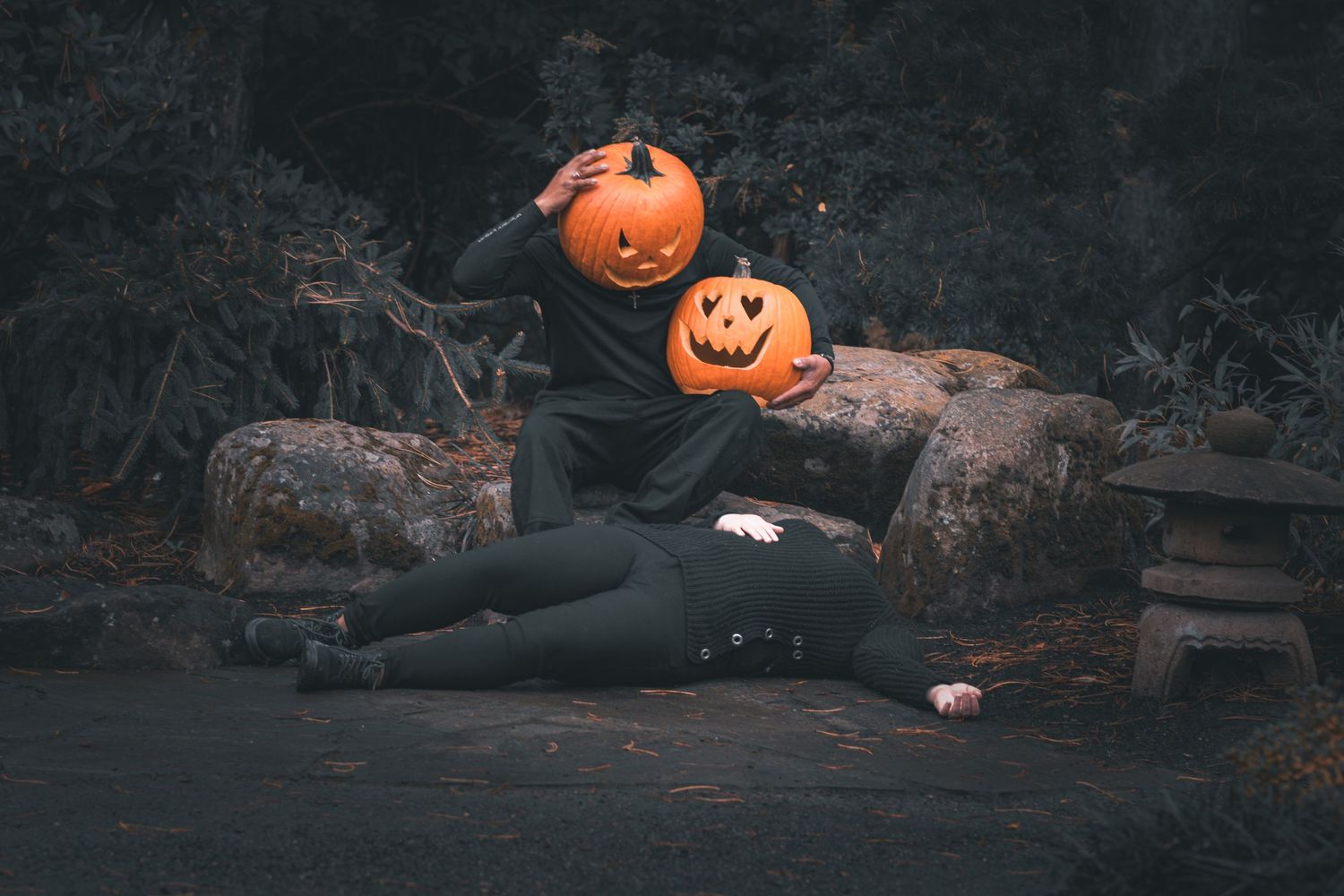 Jack-o-lantern pumpkin head figure sitting on rustic wooden logs in dark moody setting.