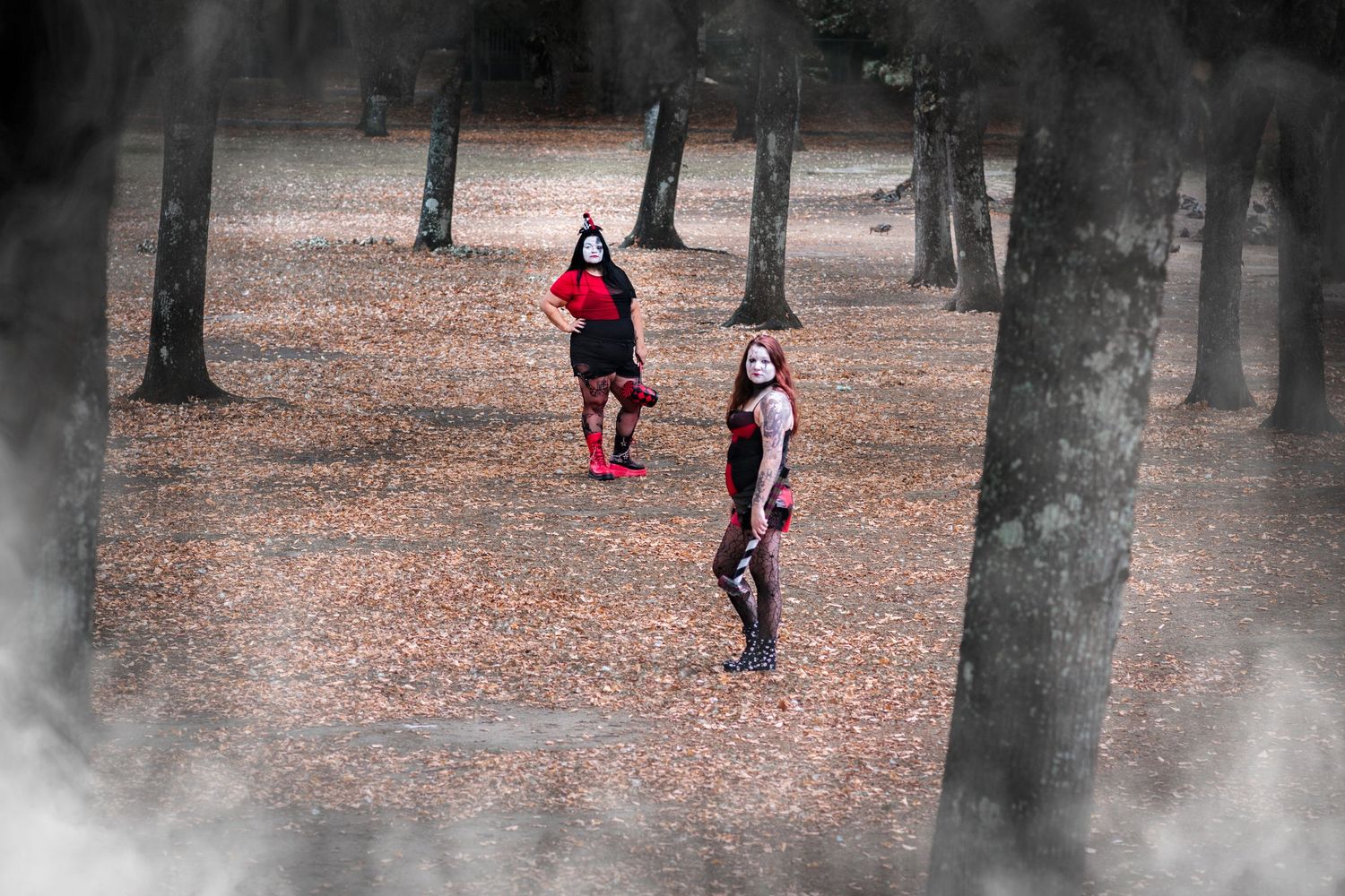 People walking through a foggy forest with fallen autumn leaves covering the ground and tall trees all around.