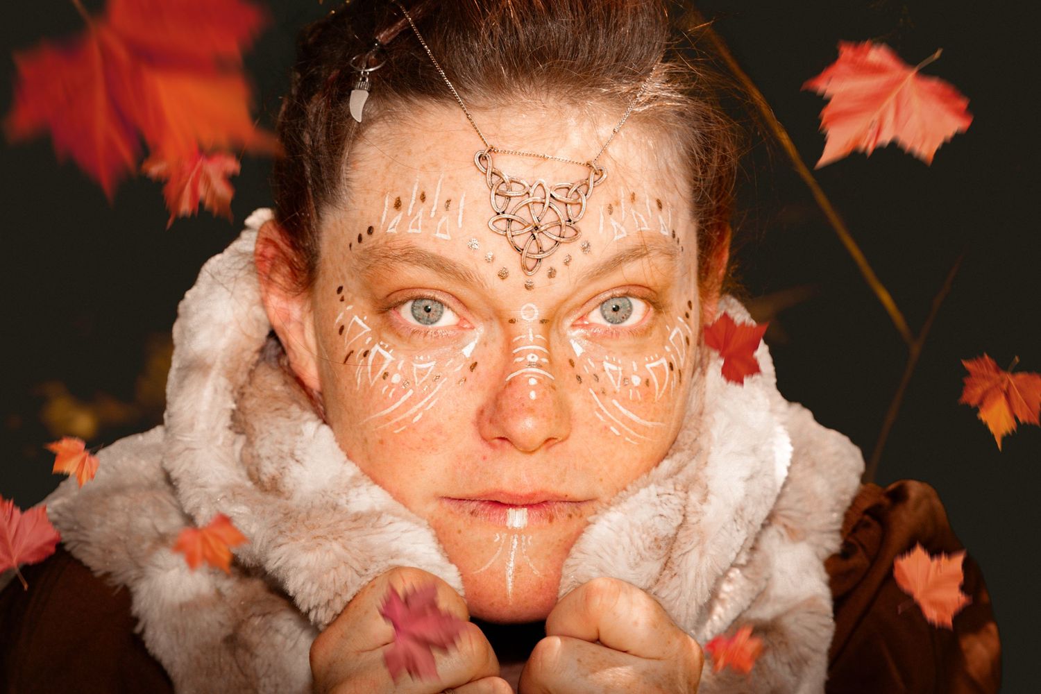 Woman with autumn-themed face paint and fur collar surrounded by falling red and orange maple leaves.
