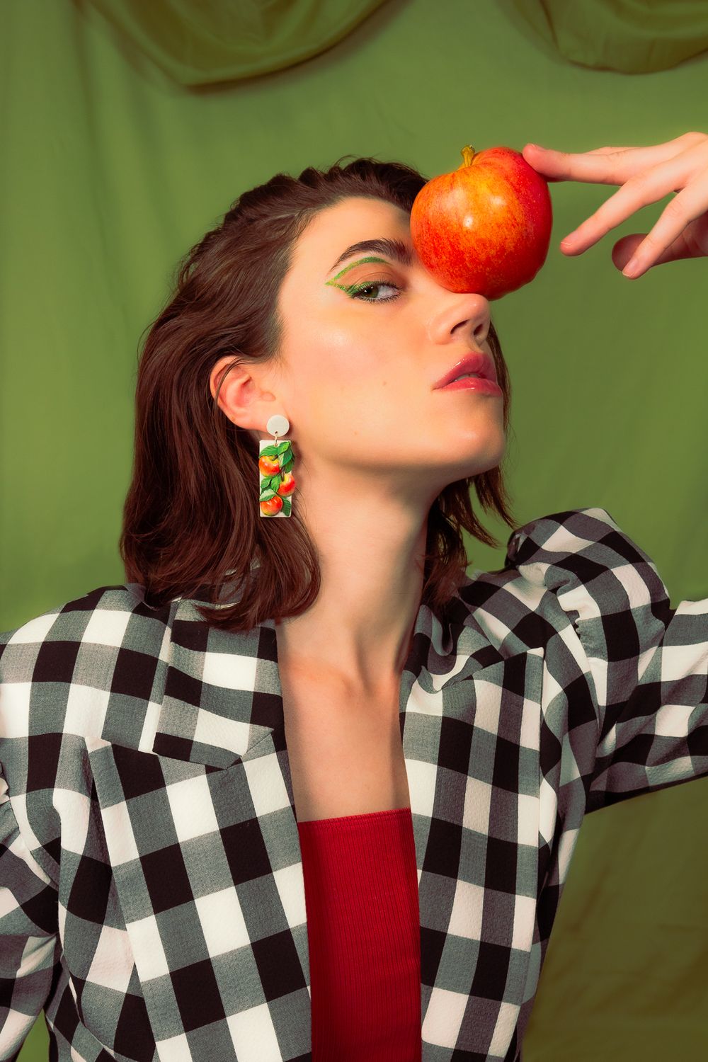 Fashion photo with black and white checkered jacket and red apple against green backdrop.