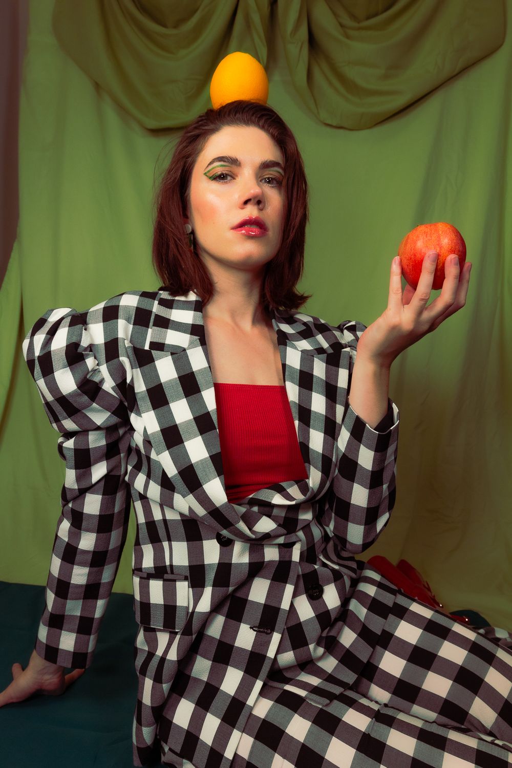 Artistic fashion shot featuring checkered outfit and balancing oranges and apples.
