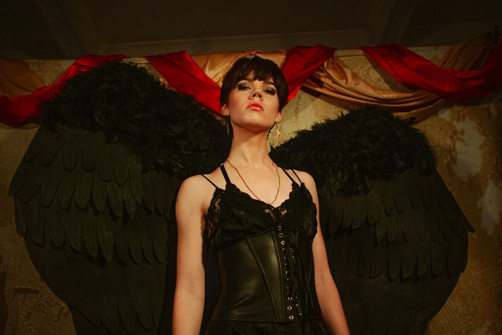 Gothic portrait featuring black angel wings and corset against red backdrop.