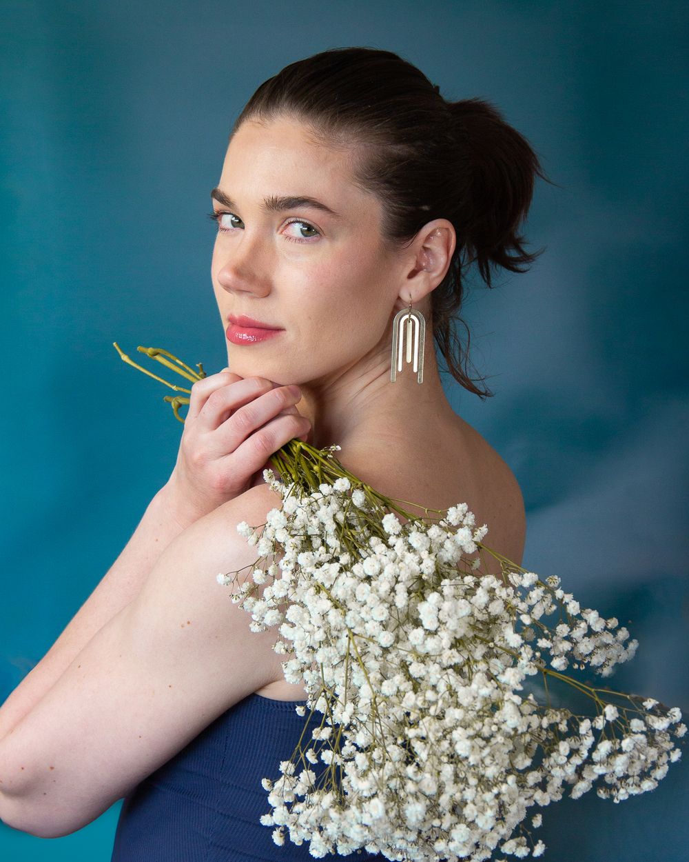 Elegant portrait with baby's breath flowers and statement earrings against blue background.