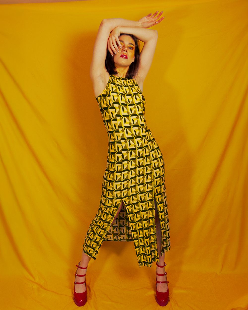 Model poses in a yellow patterned dress against vibrant yellow backdrop with red platform shoes.