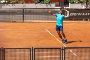 Tennis player serving on clay court with Dunlop advertising visible in background.