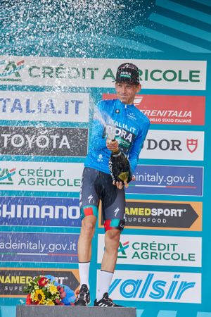 Cycling champion celebrates victory on podium with champagne spray at Italian race.