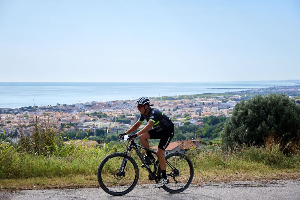 Mountain biker rides along scenic hilltop overlooking coastal city below.