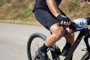 Close-up shot of a cyclist's legs and bike pedal on a dirt road.