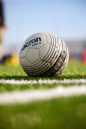 Close-up of white Macron soccer ball on grass field with white line marking.