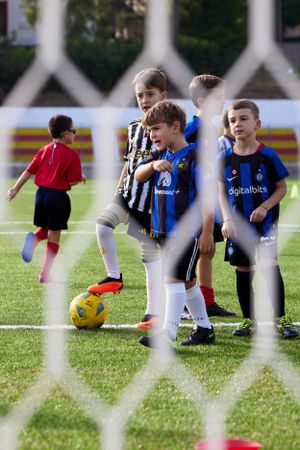 Young soccer players in different team jerseys prepare for game seen through goal netting.