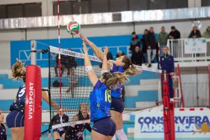 Players reach for the volleyball above the net during competitive indoor game action.