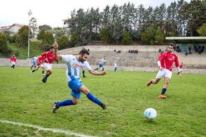 Amateur soccer players in red and blue uniforms compete for ball during match.